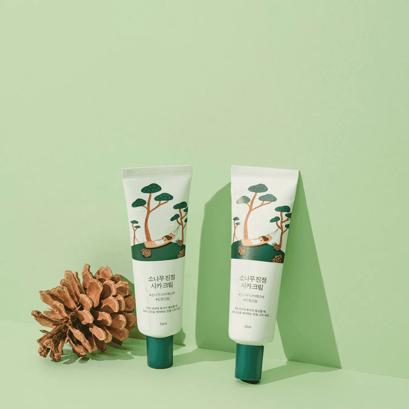 Two skincare products with a pine cone on a green background